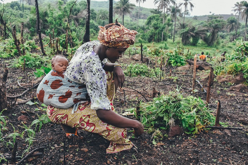 African woman working in the field with her baby on back
